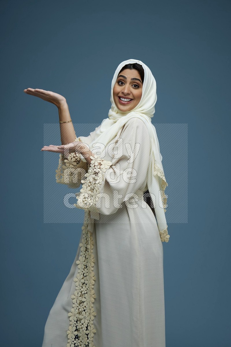 A Saudi woman pointing in a blue background wearing an off-white Abaya Hijab