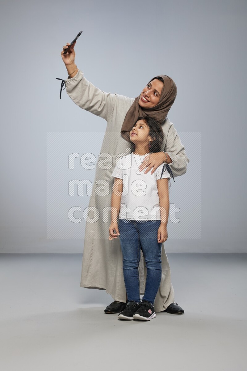 A girl standing taking selfie with her mother on gray background