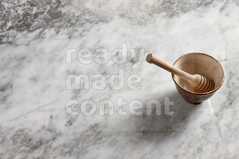 Decorative Pottery Bowl with wooden honey handle in it, on grey marble flooring, 65 degree angle