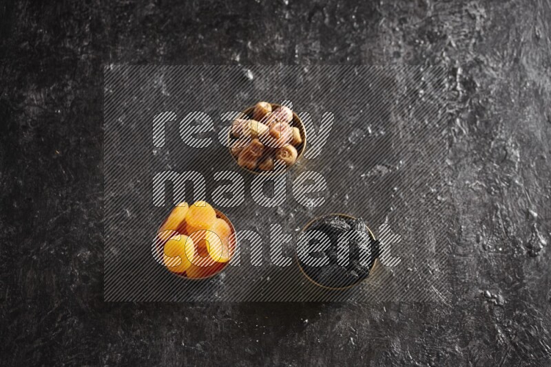 Dried fruits in metal bowls in a dark setup
