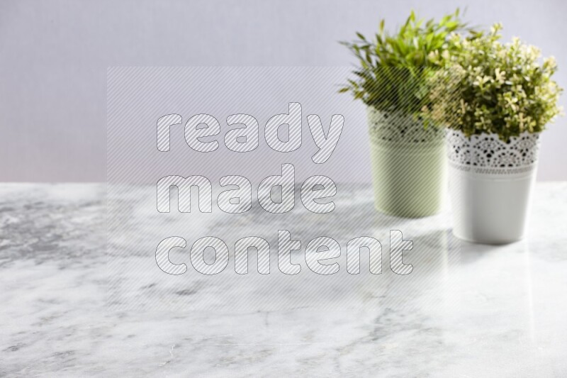 Two different artificial plants in white and green decorative pot on grey marble background
