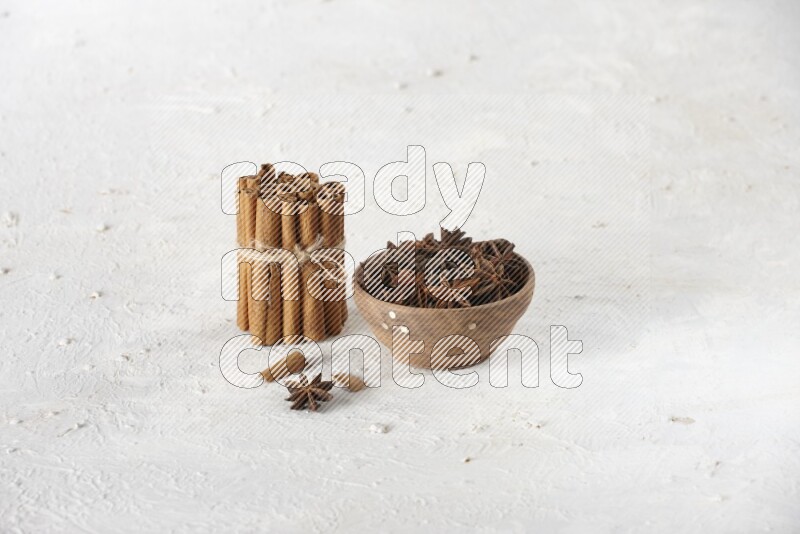 A stacked and bounded cinnamon sticks and a wooden bowl full of star anise on a white background