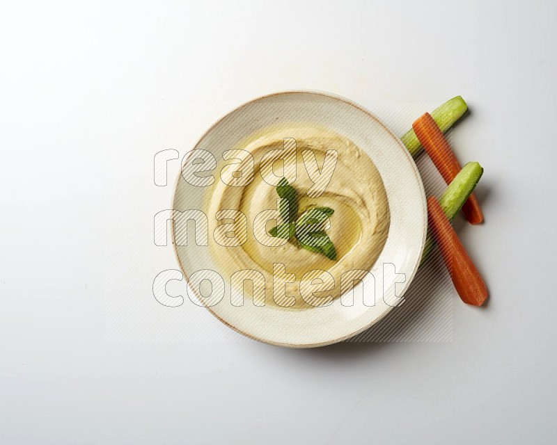 Hummus in a pottry plate garnished with mint  on a white background