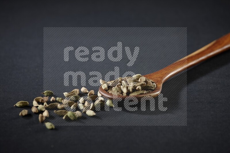 A wooden ladle full of cardamom on black flooring