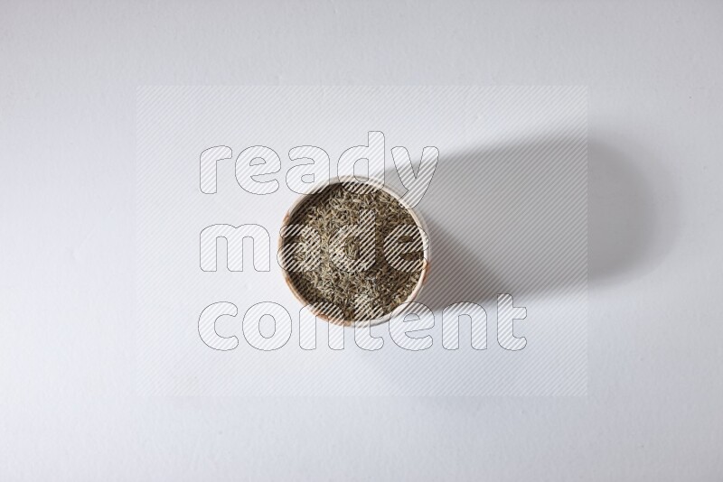 وعاء بيج ممتلئ بحبوب الكمون على خلفية بيضاء