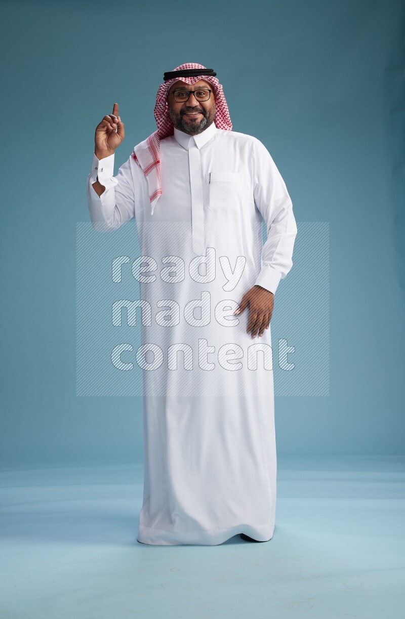 Saudi Man with shimag Standing Interacting with the camera on blue background