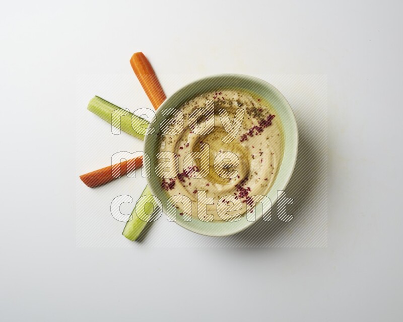 Hummus in a green plate garnished with zattar & sumak on a white background
