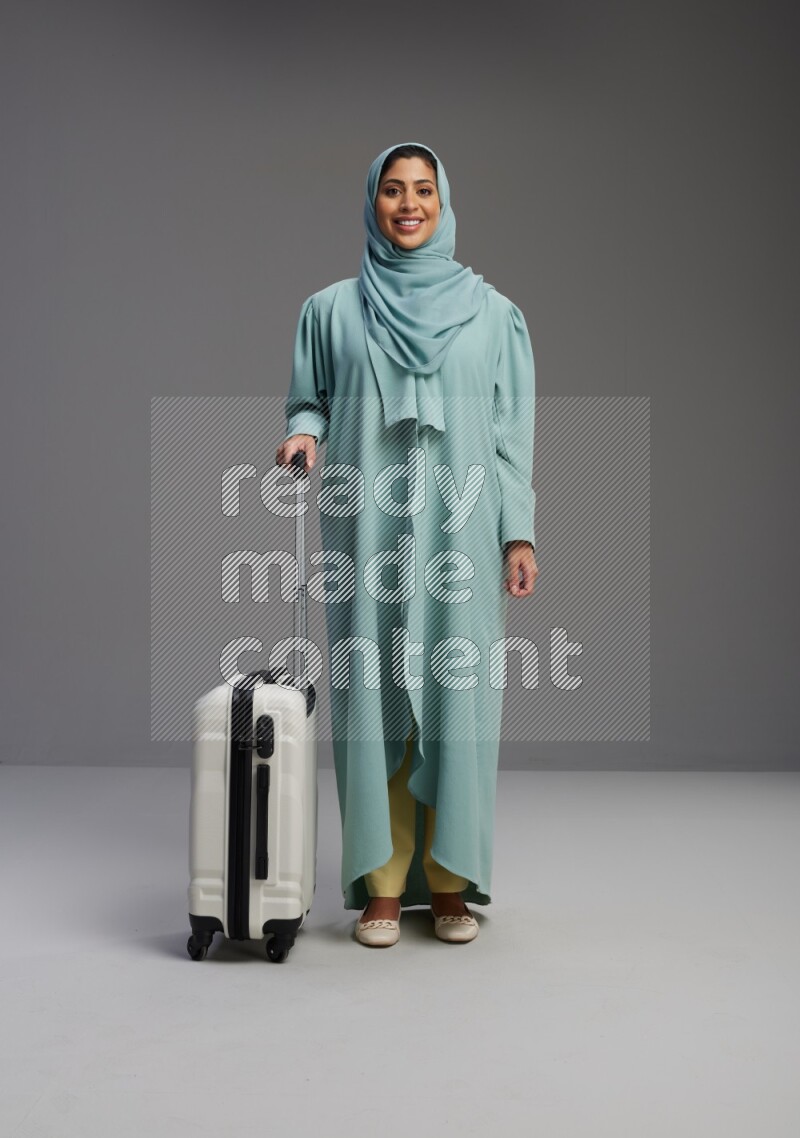 Saudi Woman wearing Abaya standing holding Travel bag on Gray background