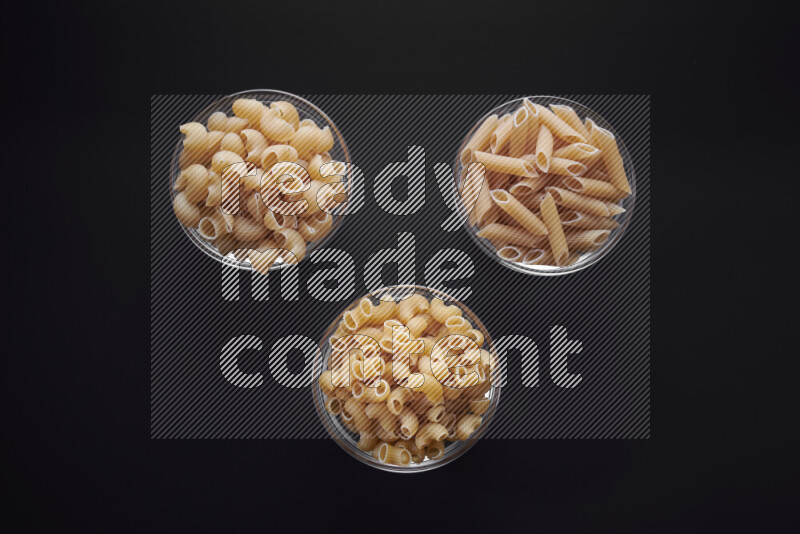 Different pasta types in glass bowls on black background