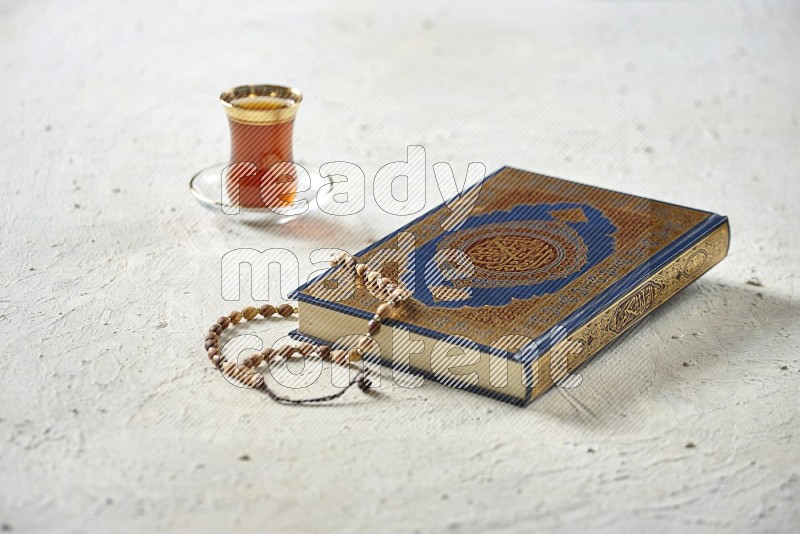 Quran with dates, prayer beads and different drinks on textured white background