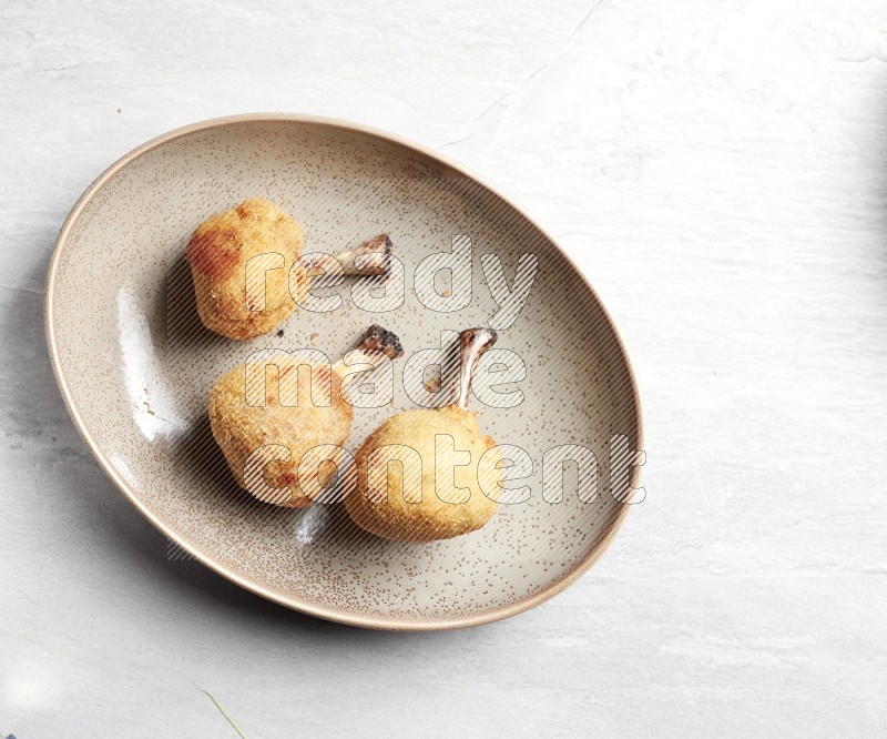 breaded drumstick on oval beige pottery plate on grey textured countertop