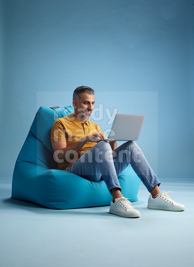 A man sitting on a blue beanbag and working on laptop