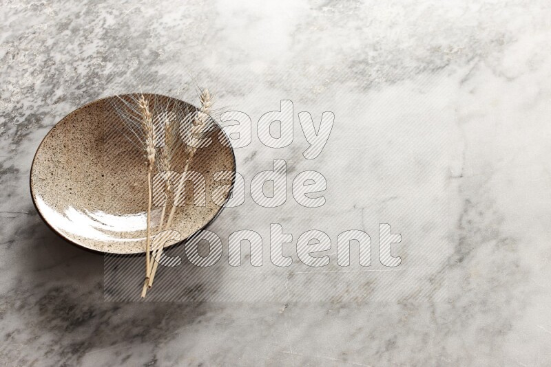 Wheat stalks on multicolored pottery plate on grey marble background