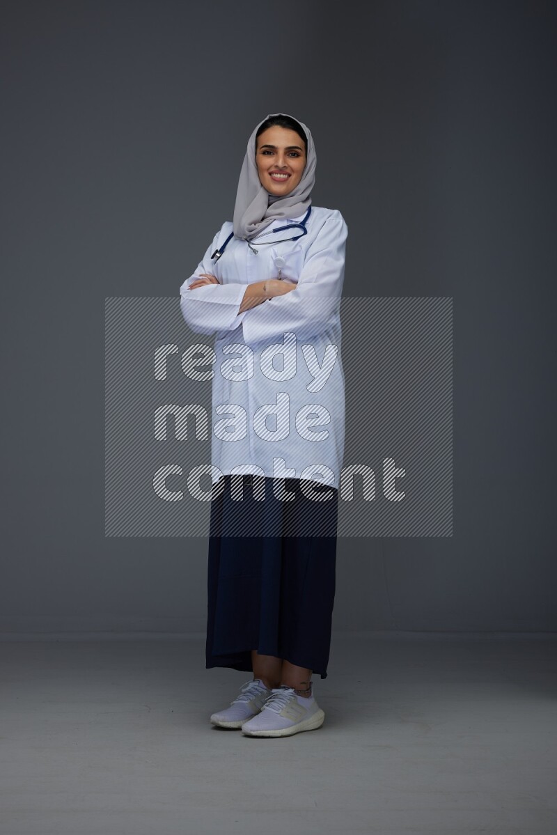 A female doctor wearing a light gray head scarf standing on grey background.