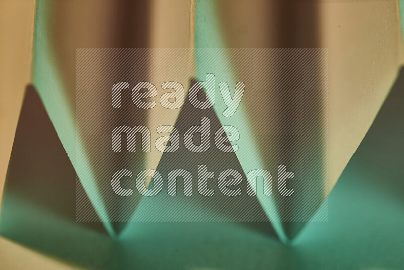 A close-up abstract image showing sharp geometric paper folds in green gradients and warm tones