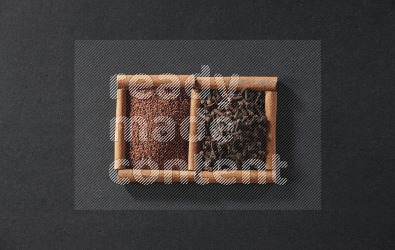 مربعان من أعواد القرفة ممتلئان بحب الرشاد والقرنفل علي خلفية سوداء