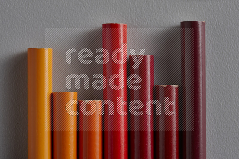 A collection of colored pencils arranged showcasing a gradient of orange and red hues on grey background