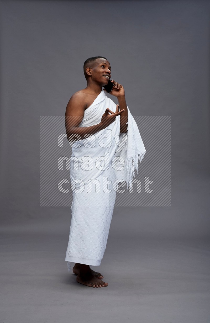 A man wearing Ehram Standing talking on phone on gray background