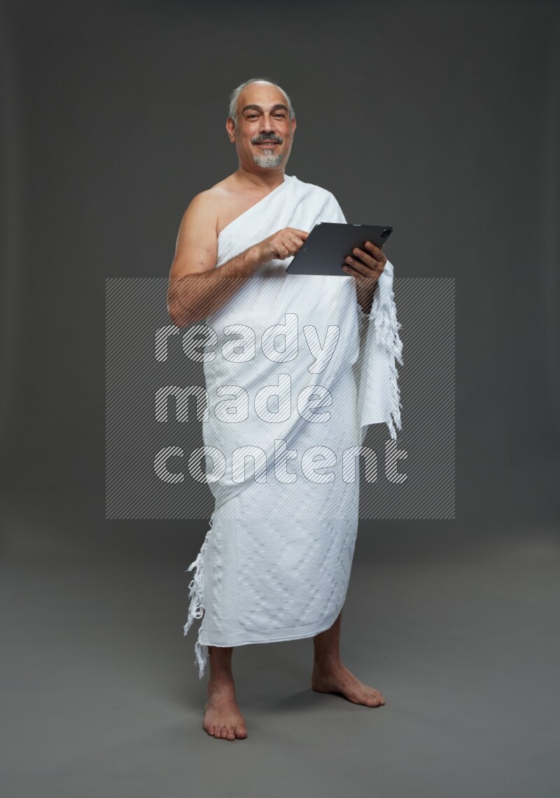 A man wearing Ehram Standing working on tablet on gray background