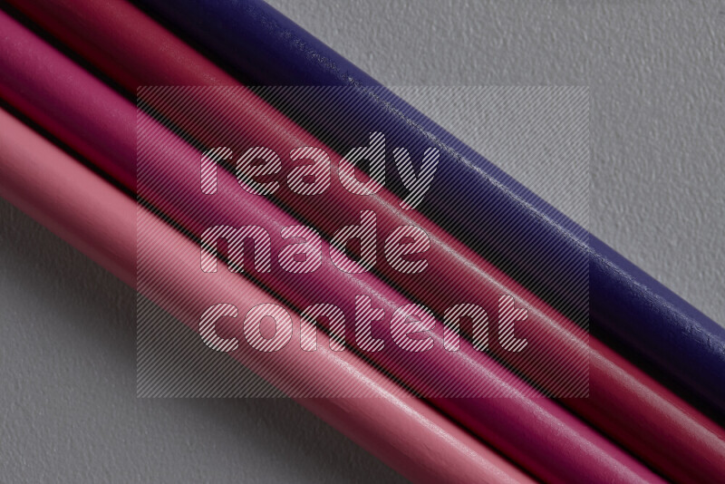 A collection of sharpened colored pencils arranged showcasing a gradient of pink and purple hues on grey background