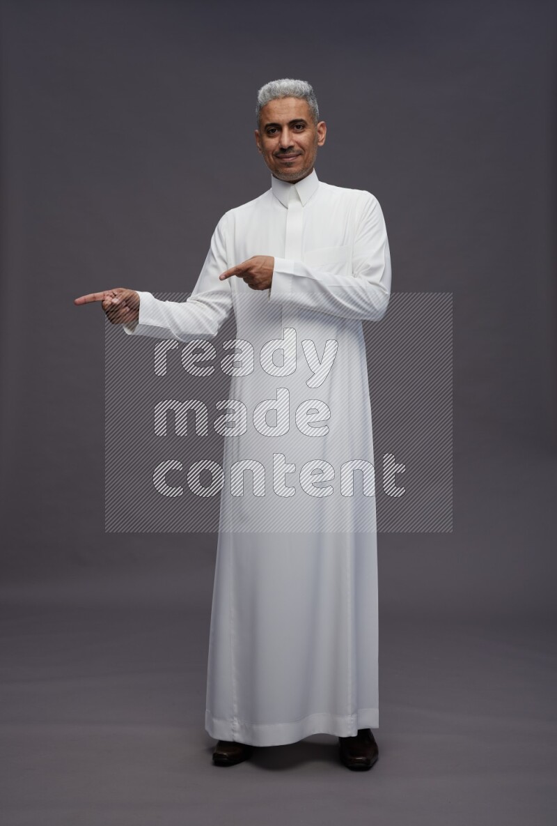 Saudi man wearing thob standing interacting with the camera on gray background