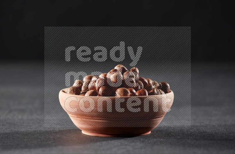 A wooden bowl full of peeled hazelnuts on a black background in different angles