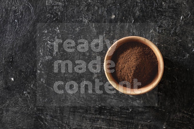 A wooden bowl full of cloves powder on a textured black flooring