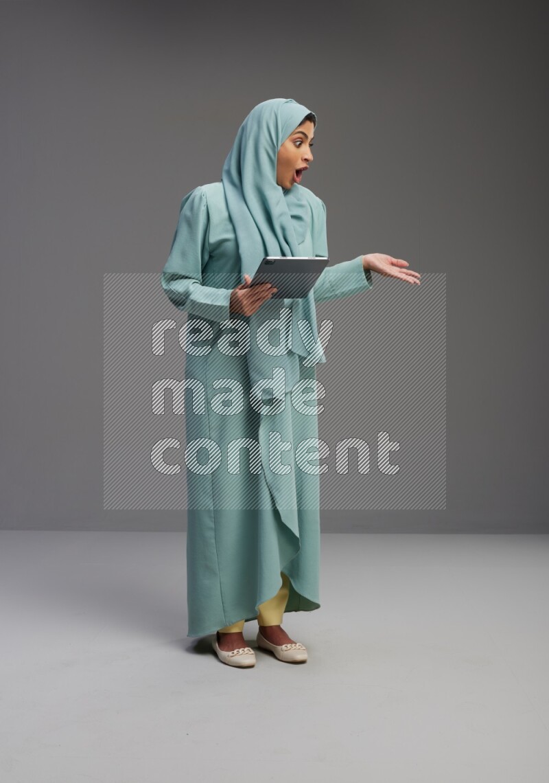 Saudi Woman wearing Abaya standing working on tablet on Gray background