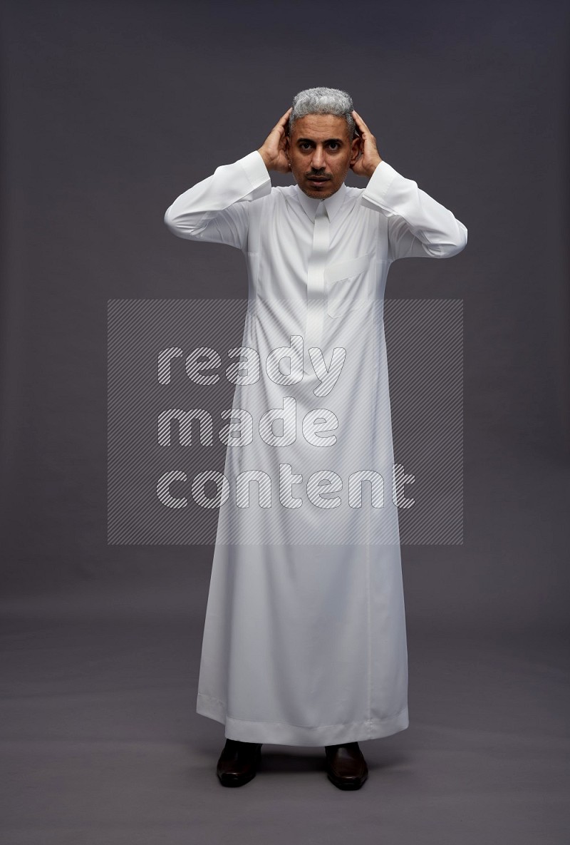 Saudi man wearing thob standing hands behind head on gray background