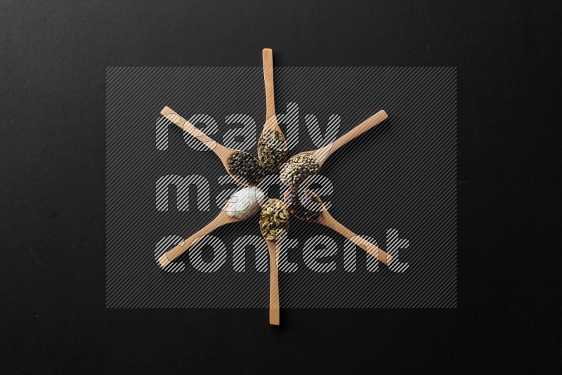 wooden spoons filled with white peppers, cloves, cardamom, salt, black peppers and basil on black flooring and shaped like a clock