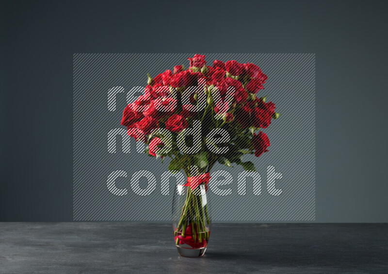 An arrangement of vivid red roses tightly bound with a red ribbon in a glass vase on black marble background