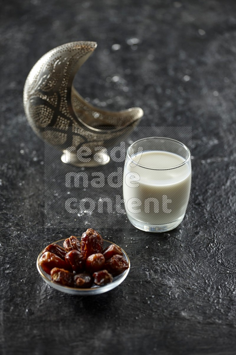 A silver lantern with drinks, dates, nuts, prayer beads and quran on textured black background