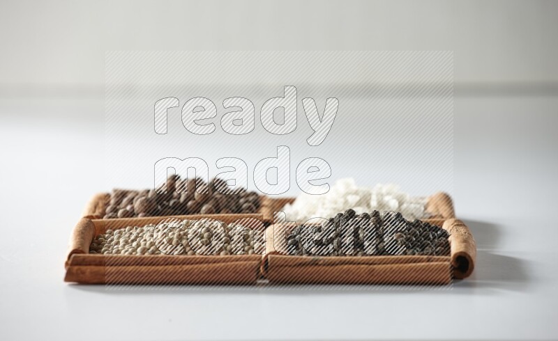 4 squares of cinnamon sticks full of allspice, white salt, white pepper and black pepper on white flooring