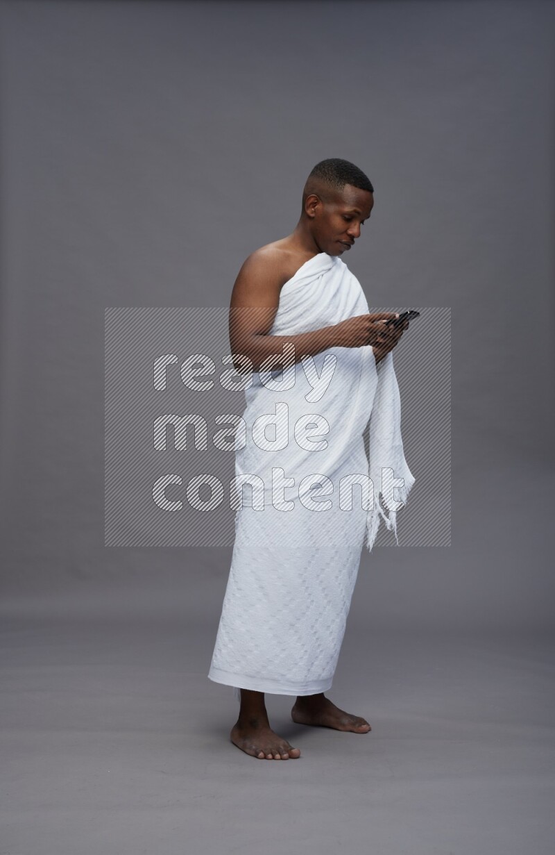 A man wearing Ehram Standing texting on phone on gray background