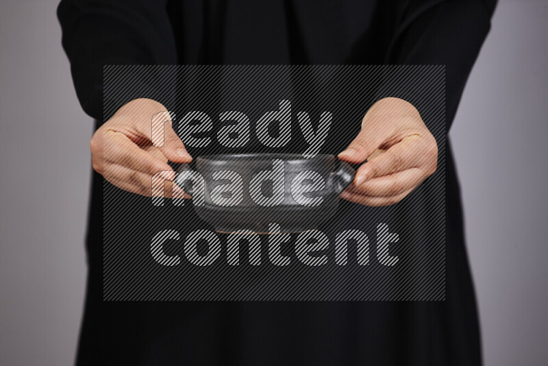 A woman in black abaya holding different pottery essentials in different positions