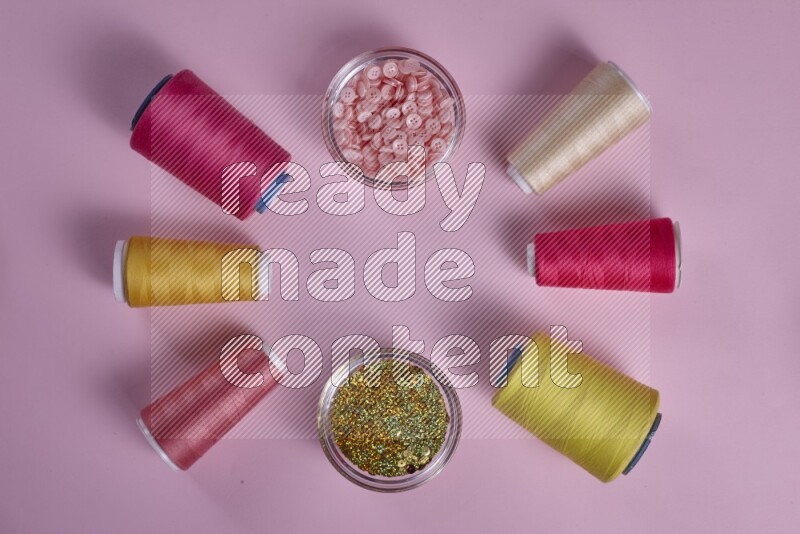 A yellow and pink collection of sewing and tailoring tools arranged on a pink background