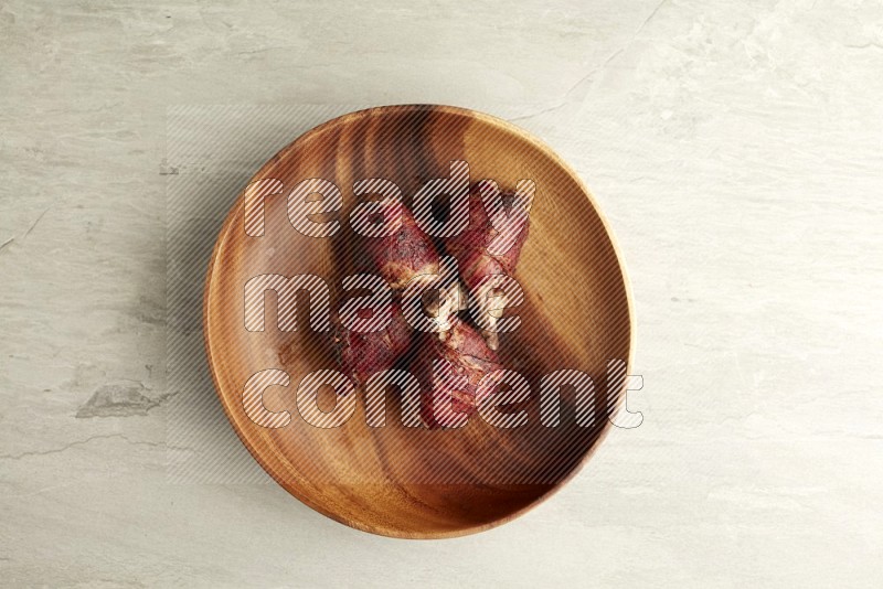 drumstick wrapped in bacon on round brown wooden plate on grey textured countertop