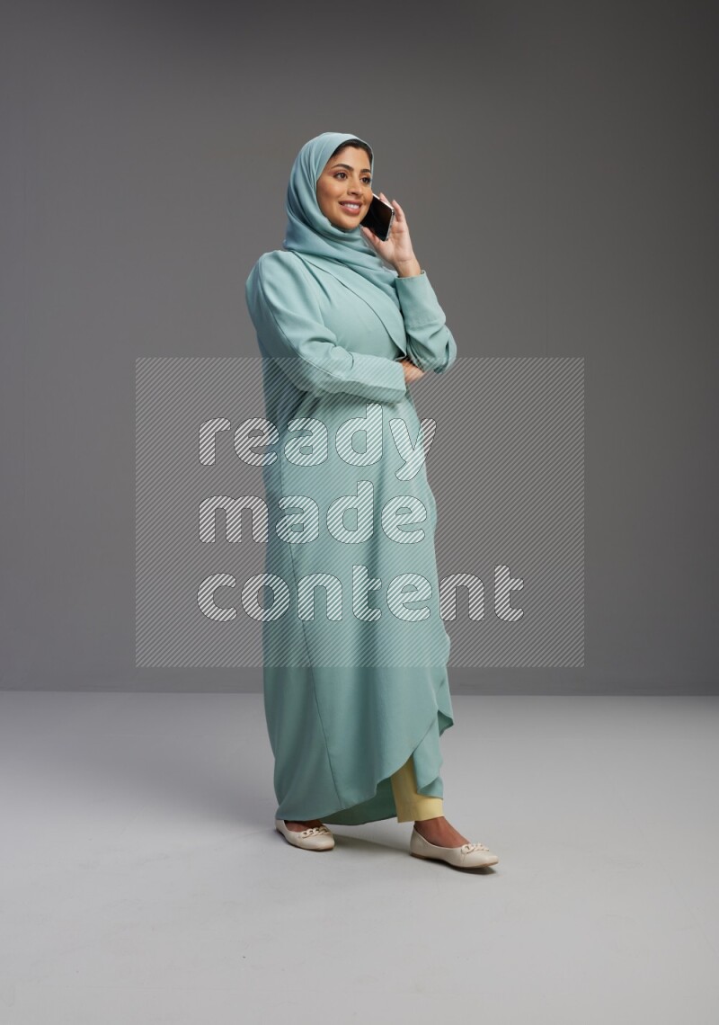Saudi Woman wearing Abaya standing talking on phone on Gray background