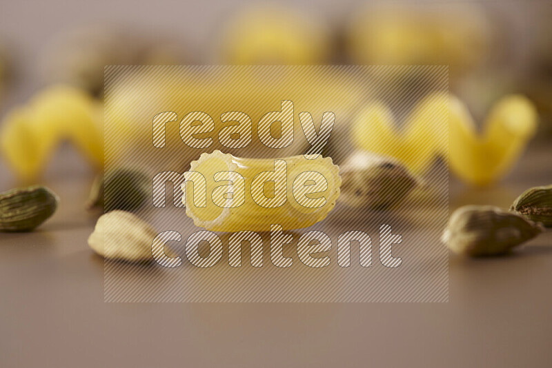 Raw pasta with different ingredients such as cherry tomatoes, garlic, onions, red chilis, black pepper, white pepper, bay laurel leaves, rosemary and cardamom on beige background