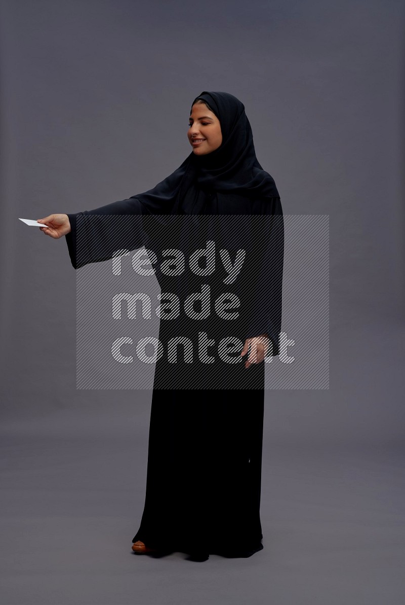 Saudi woman wearing Abaya standing holding ATM card on gray background