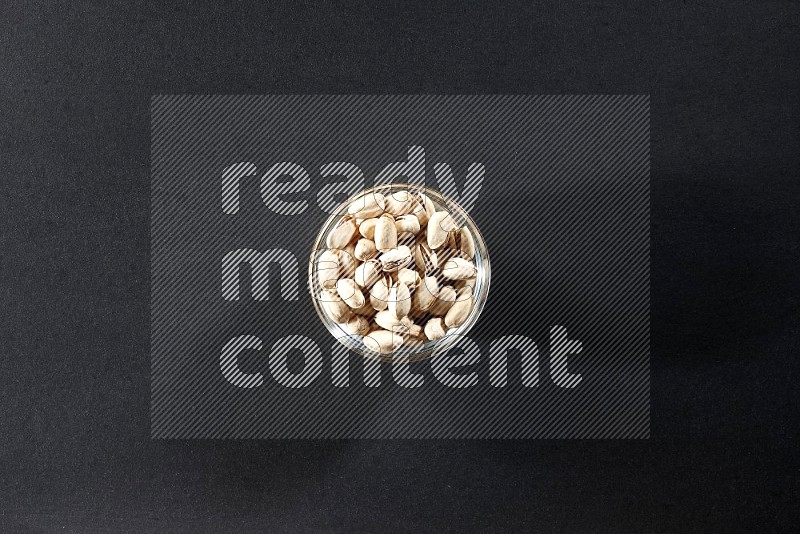 A glass bowl full of pistachios on a black background in different angles