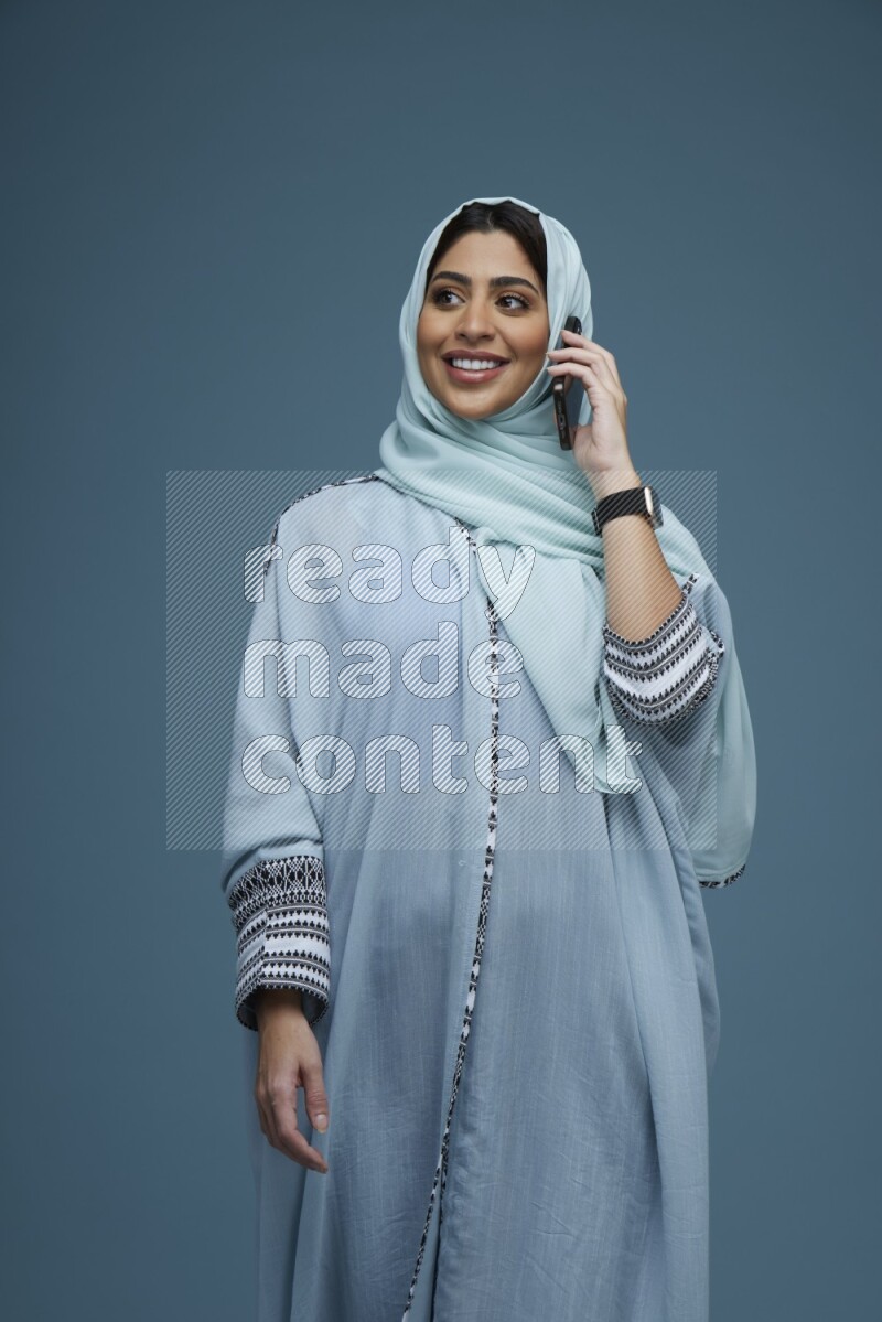 A Saudi woman having a Call in a blue background wearing blue Abaya with hijab
