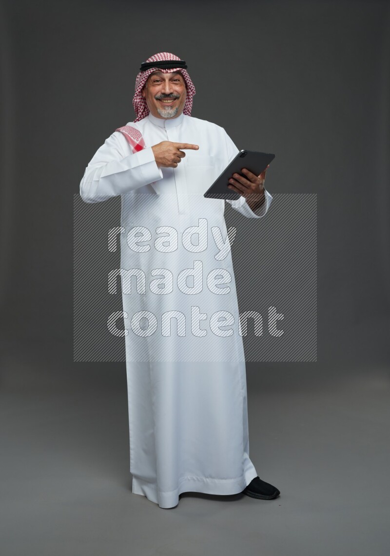 Saudi man with shomag Standing working on tablet on gray background