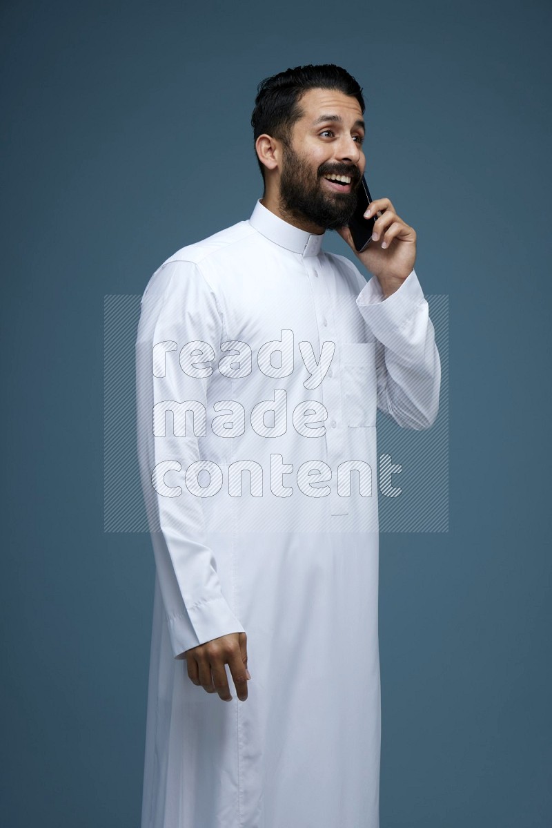 A man having a call on a blue background wearing Saudi Thob