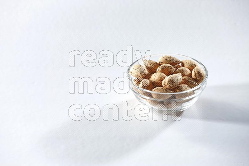 A glass bowl full of almonds on a white background in different angles