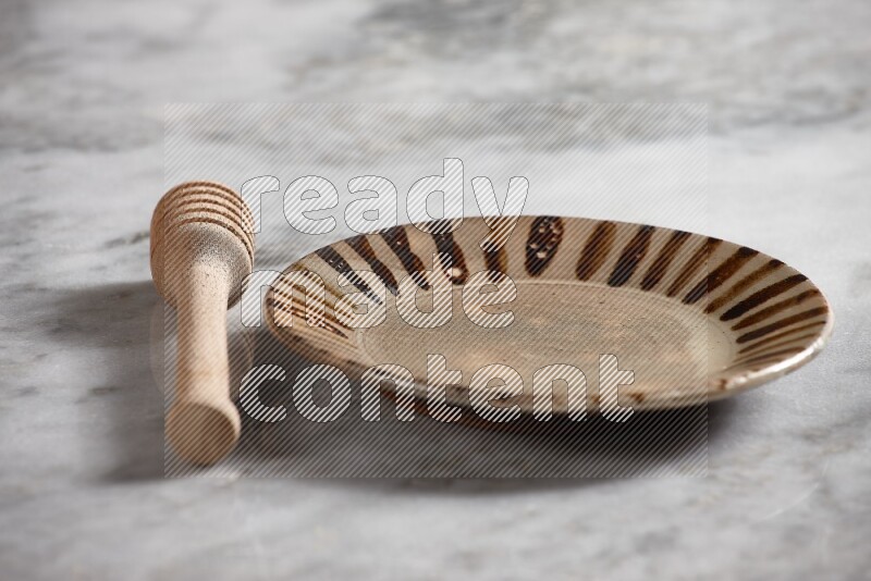 Multicolored pottery plate with wooden honey dipper on the side on grey marble background
