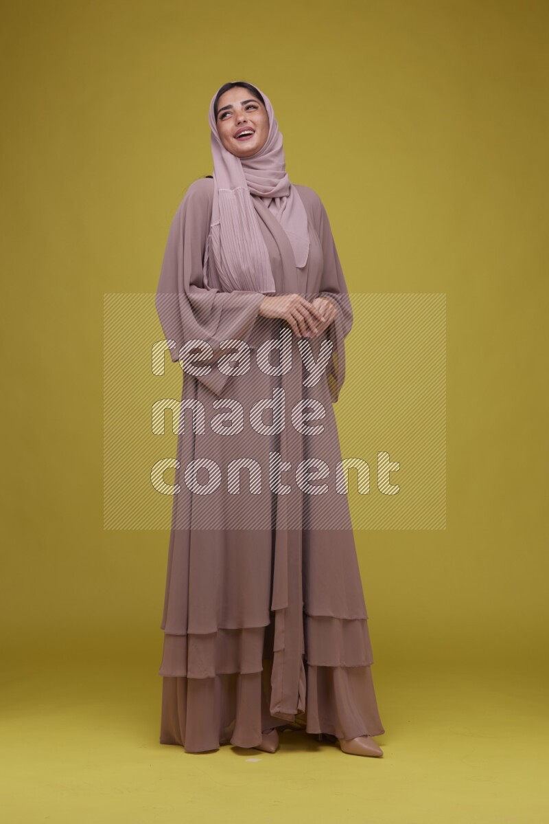 A woman Posing on a Yellow Background wearing Brown Abaya with Hijab