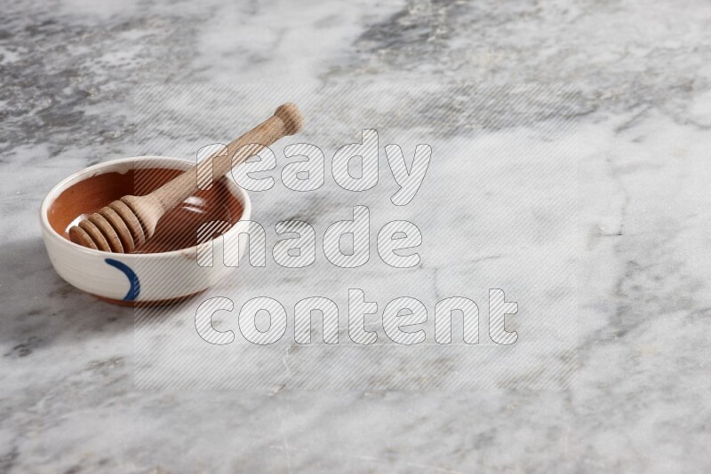 Multicolored pottery bowl with wooden honey dipper in it on grey marble background