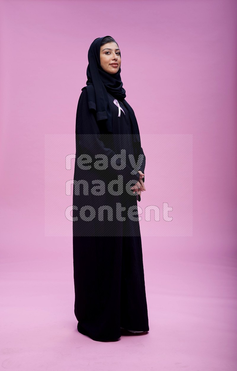 Saudi woman wearing Abaya standing with crossed arms on pink background