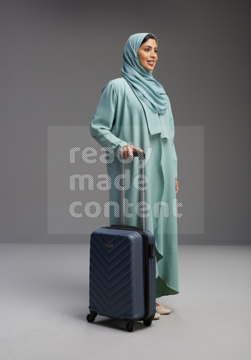Saudi Woman wearing Abaya standing holding Travel bag on Gray background